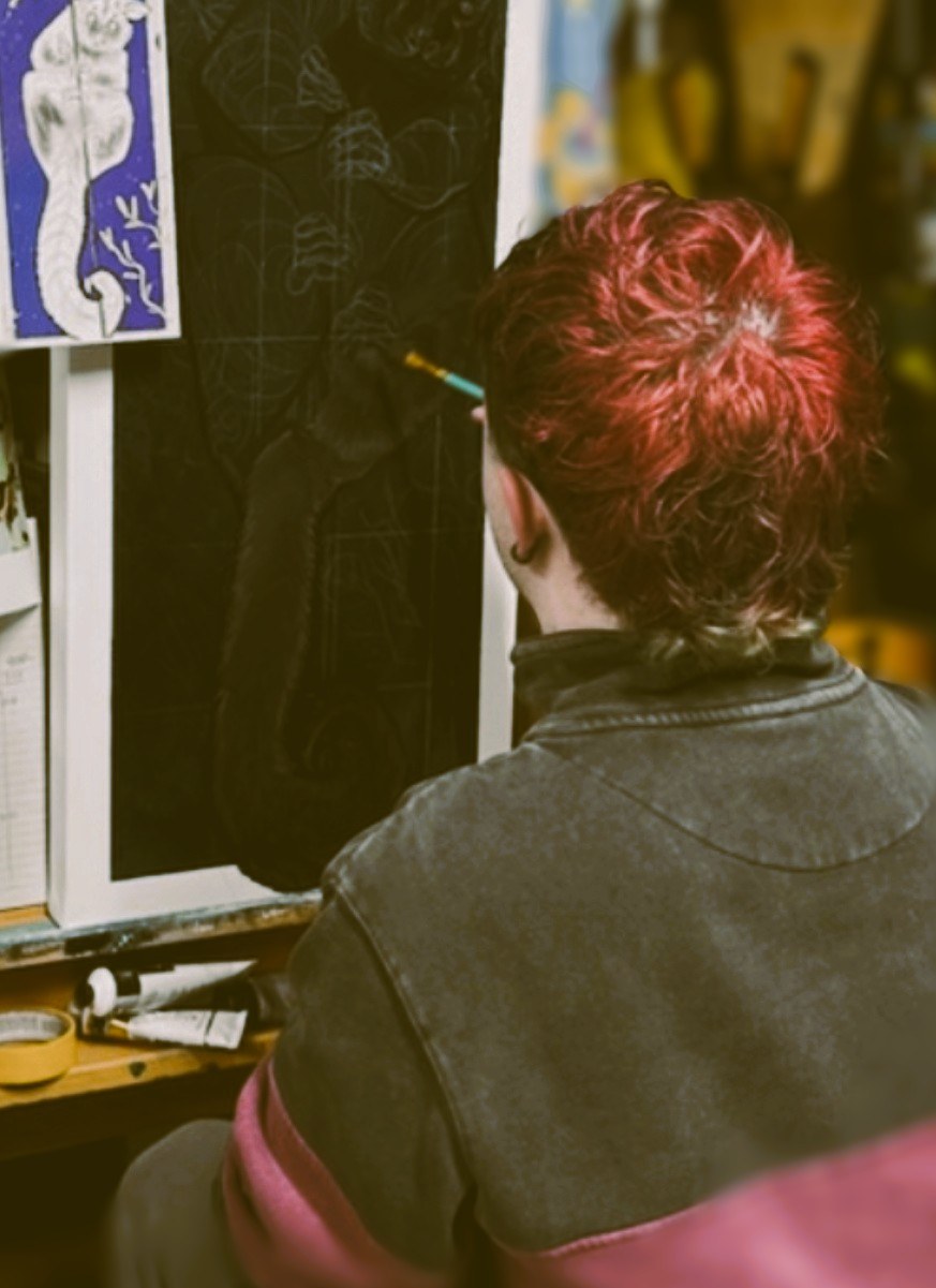 Silas painting at an easel in the studio, seen from behind