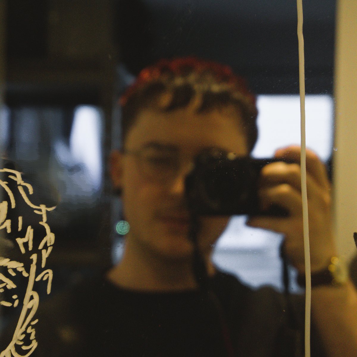 Silas Ingles, a self-portrait photographed in a mirror, camera in hand beside a paint-marker sketch