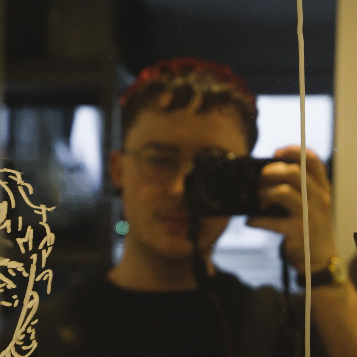 Silas Ingles, a self-portrait photographed in a mirror, camera in hand beside a paint-marker sketch